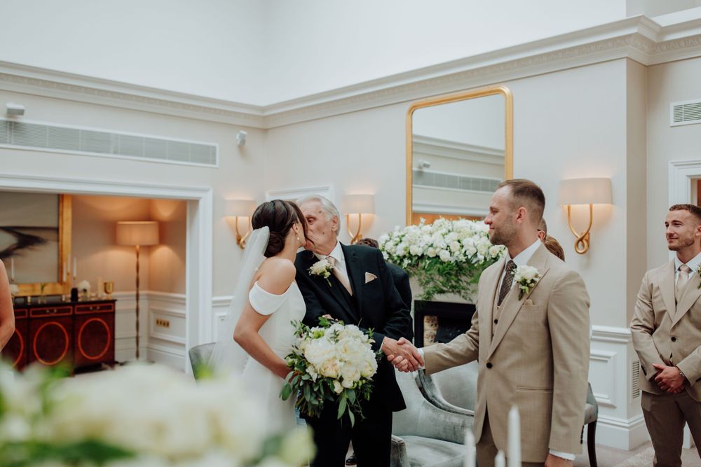 Wedding ceremony taking place in an elegant room with white walls and floral arrangements.
