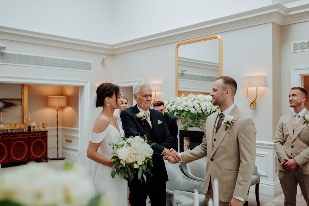 An intimate indoor wedding ceremony with white floral decor and warm lighting in an elegant room.