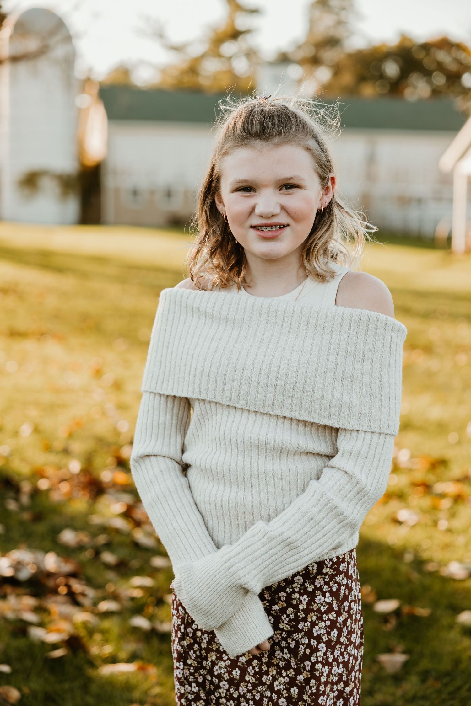 Young person in cream sweater and floral skirt poses outdoors during golden hour during family portraits with Rachel Martinez Photography.