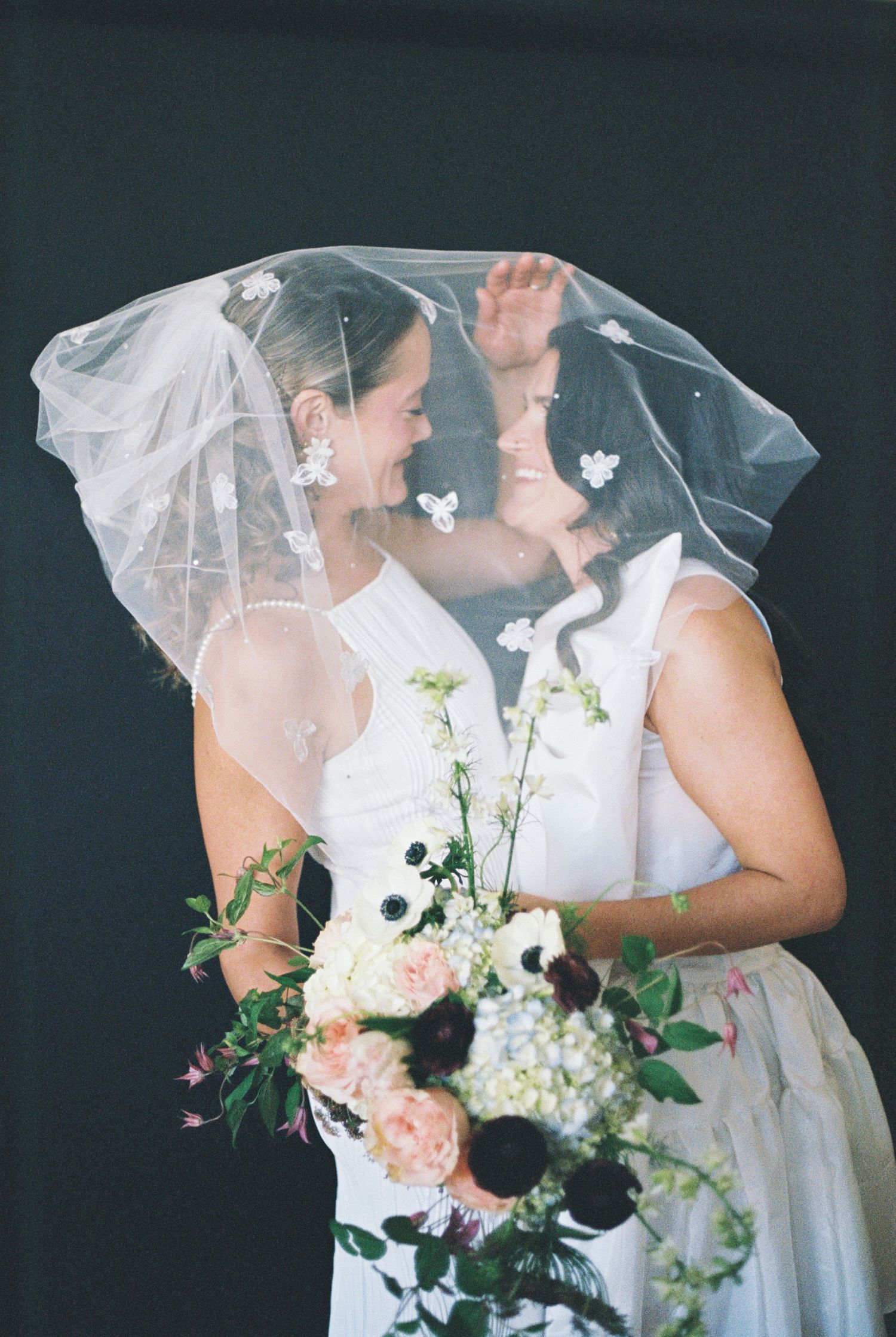 A wedding moment captured with white flowers and a flowing veil against a dark background.