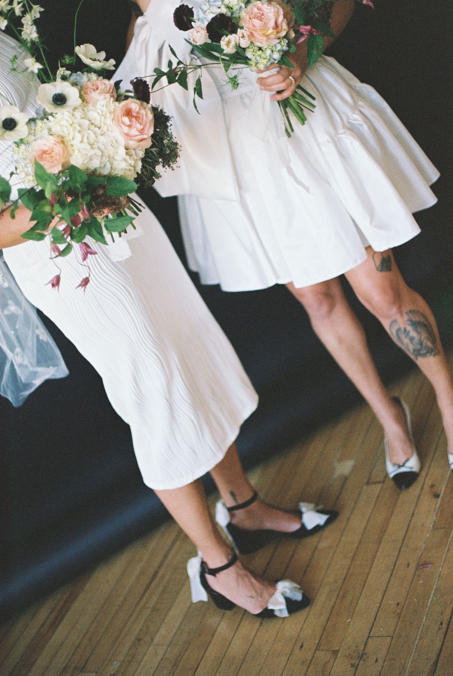 Two people in white dresses holding floral bouquets with pink and white flowers.