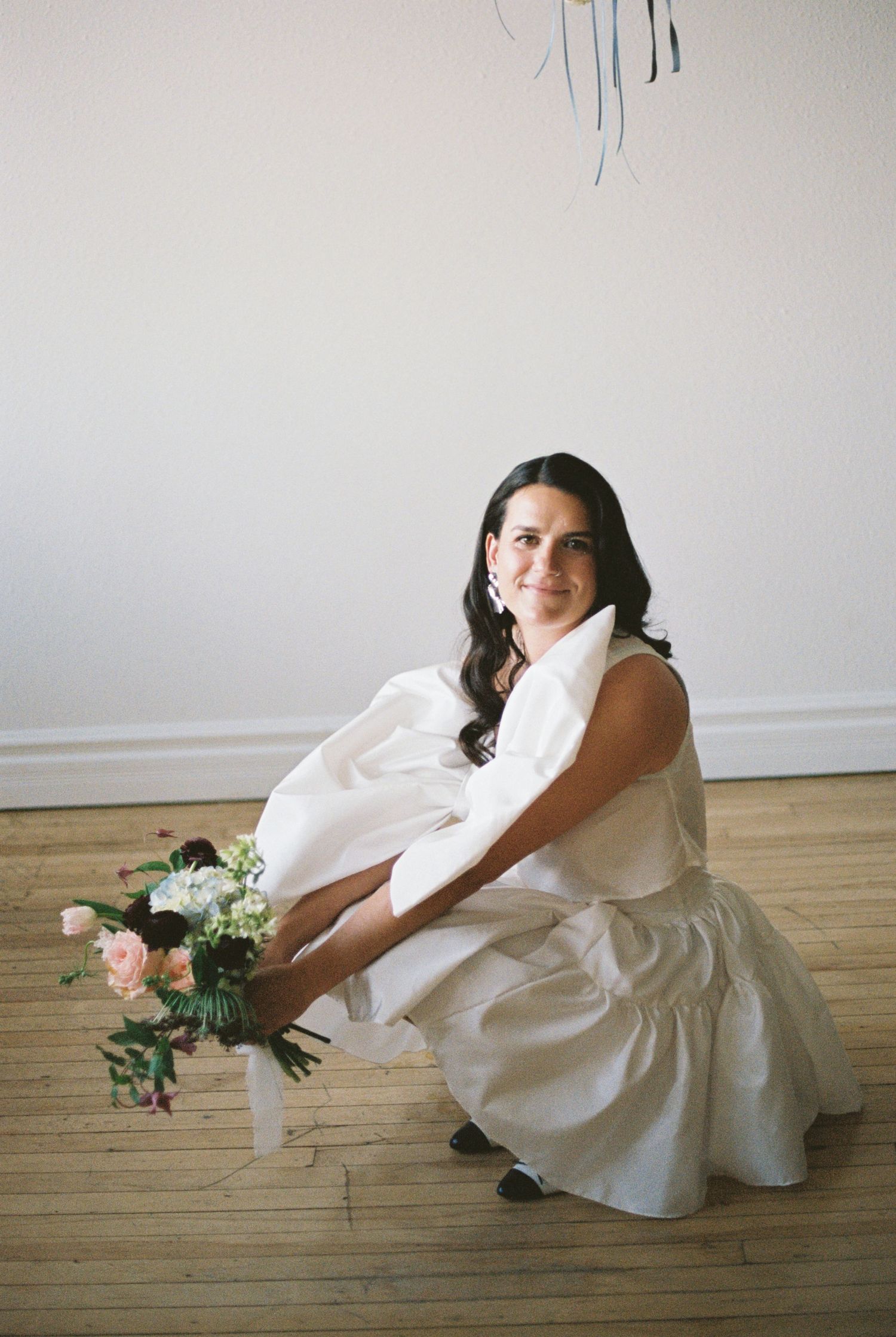 Bridal portrait in a white dress with floral details on wooden floor.