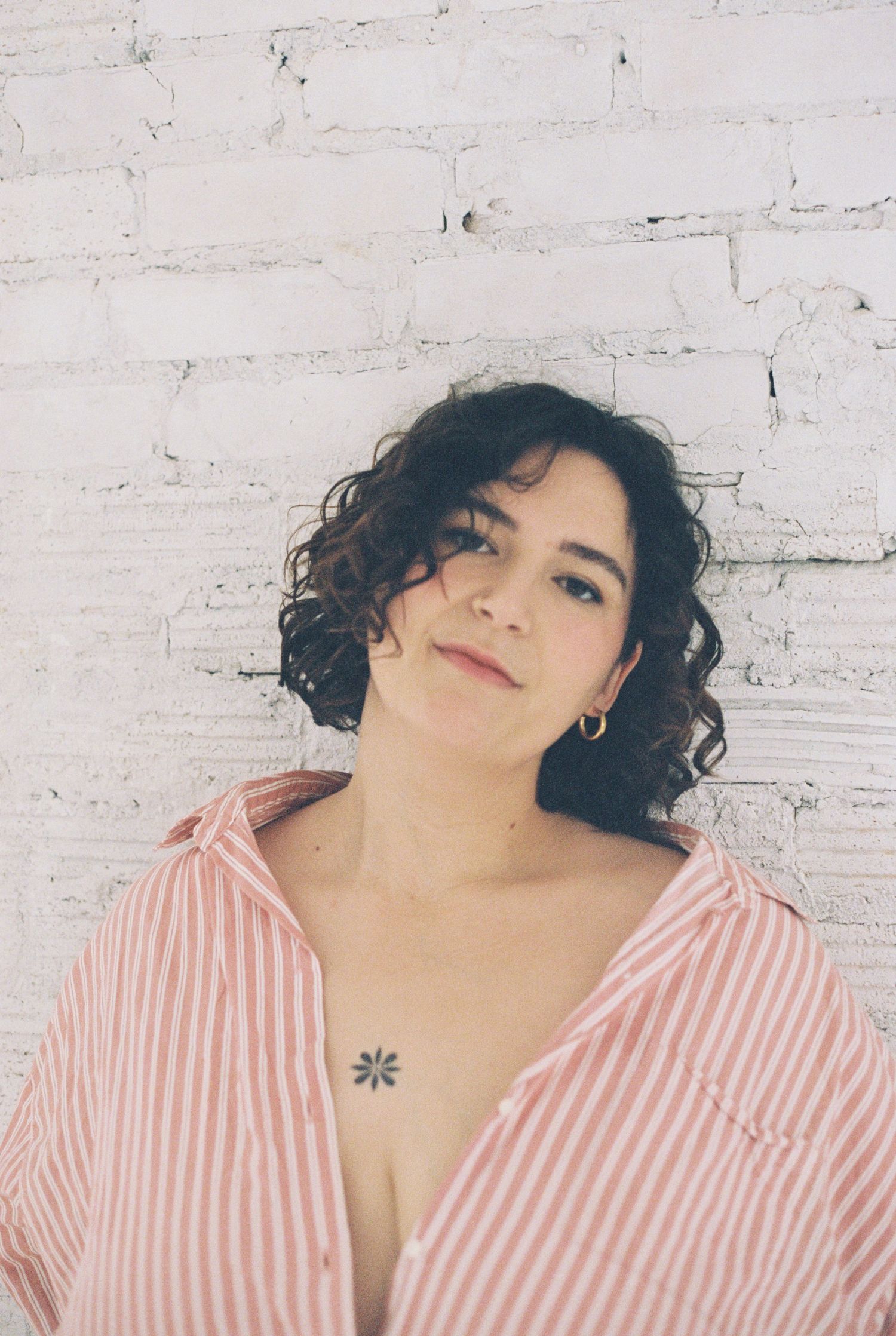 Portrait against white brick wall wearing pink striped shirt and natural curly hair.