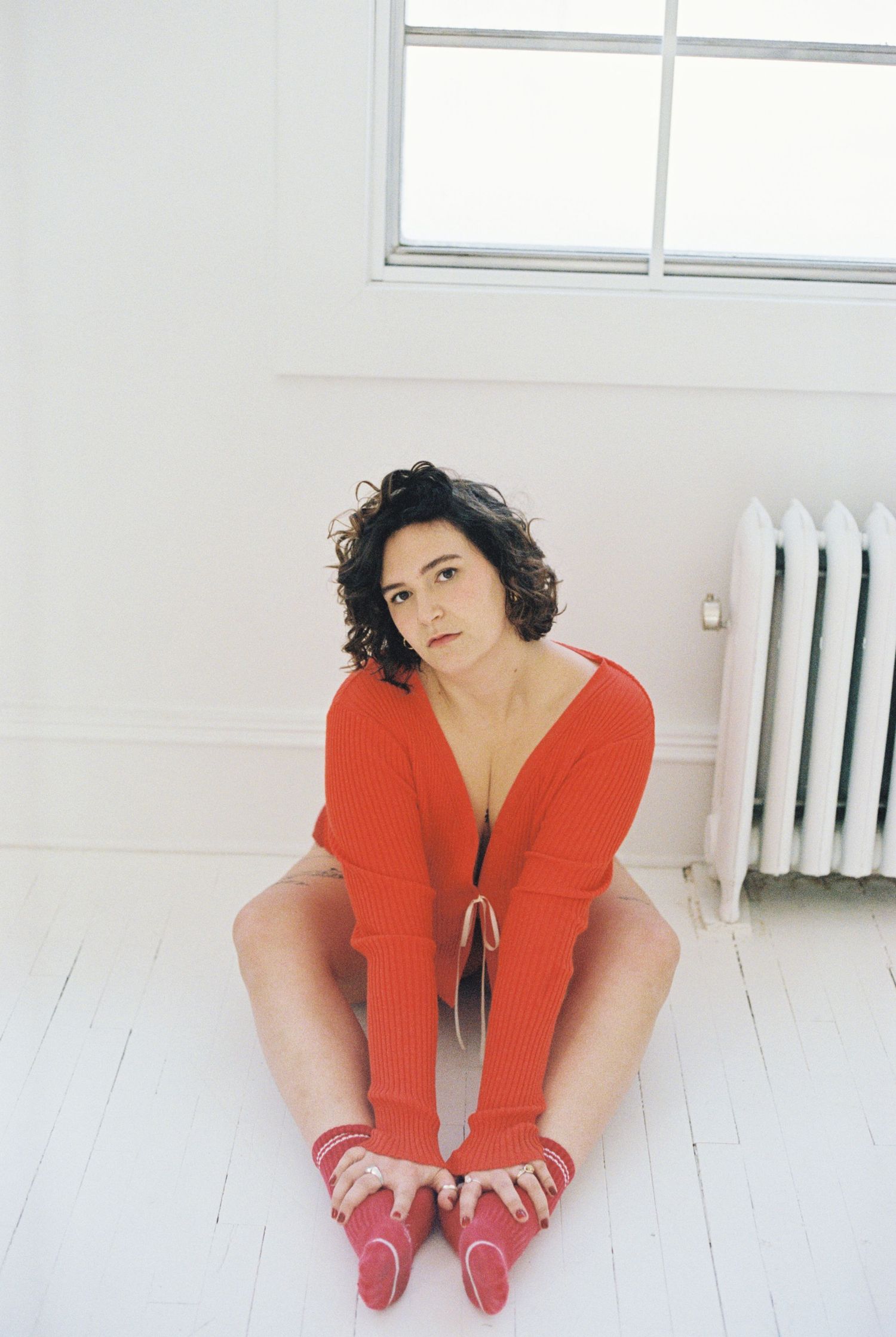 Fashion portrait in minimalist white room wearing red sweater and matching socks.