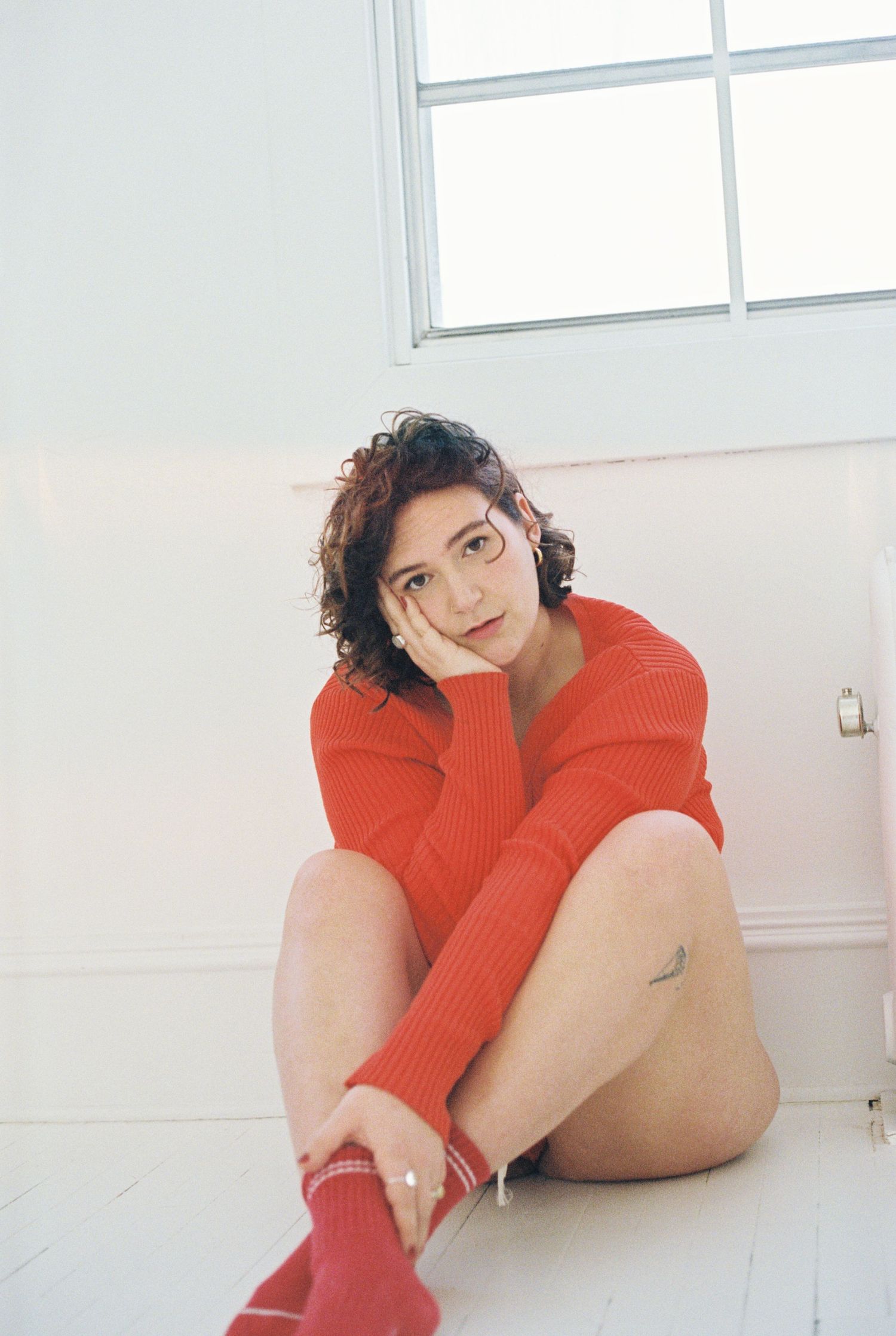 Candid portrait in red sweater sitting on white floor near window.