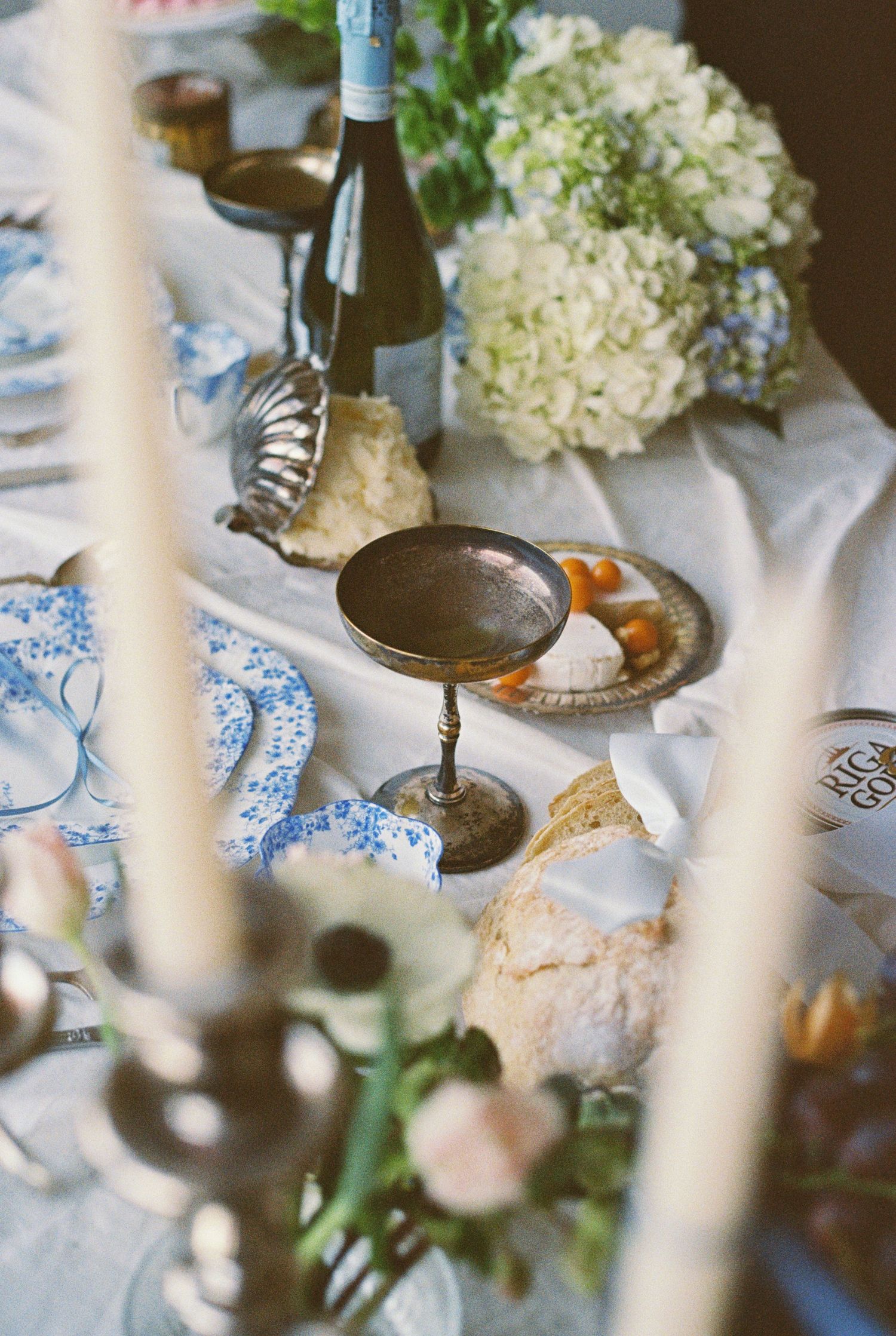 Elegant table setting with wine, hydrangeas, and candlesticks on a blue and white tablecloth.