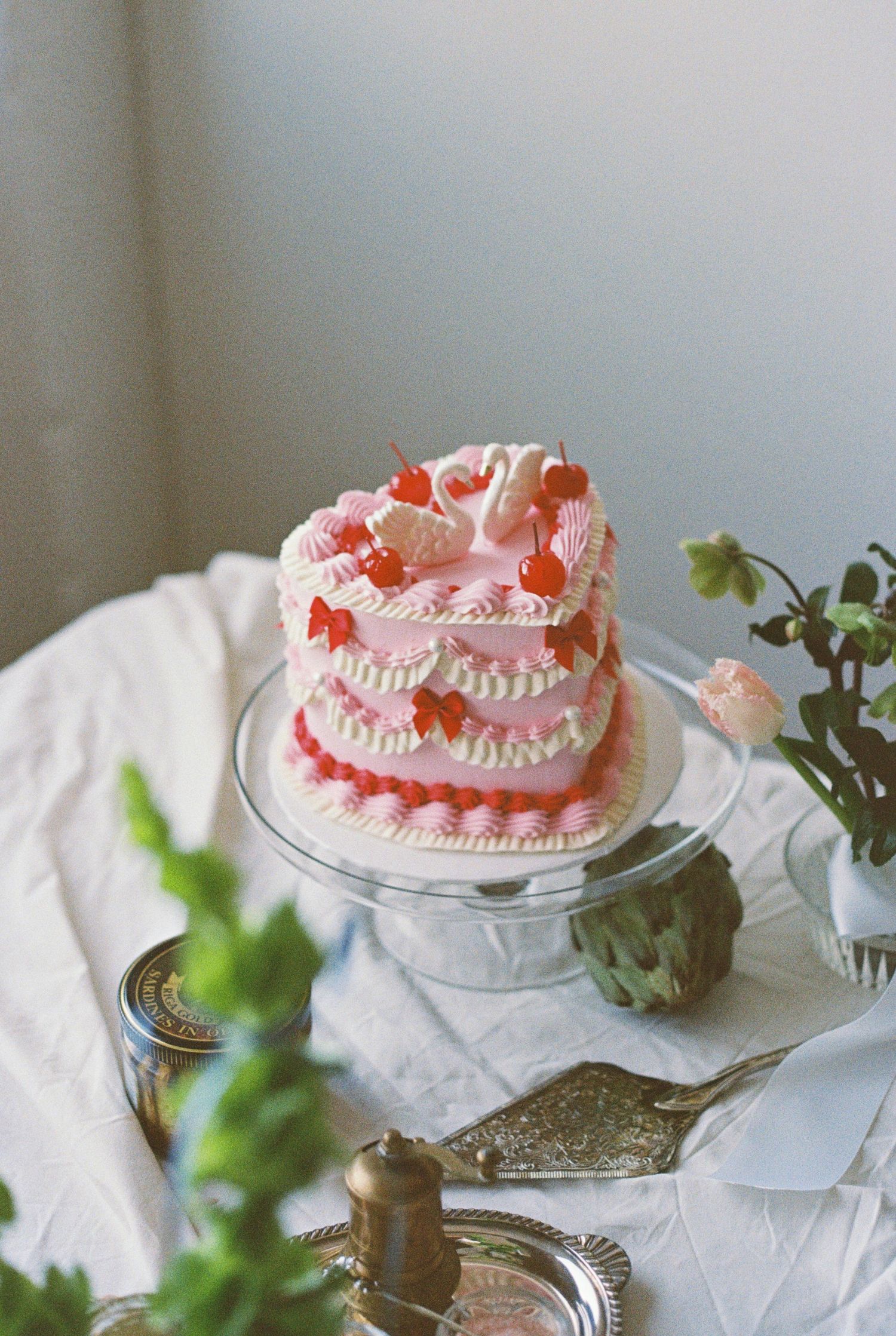 A delicate pink ruffle cake displayed on a glass cake stand with greenery accents.
