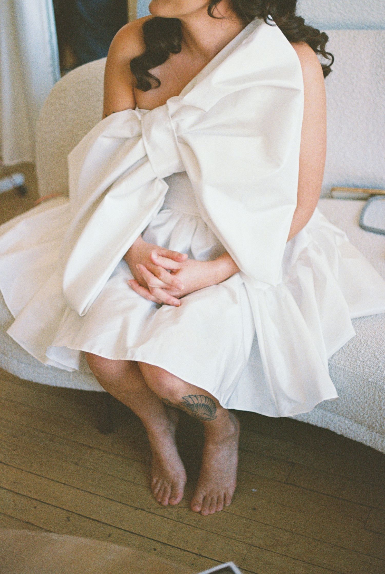 Close-up of a white bow detail on the back of a dress against wooden flooring.