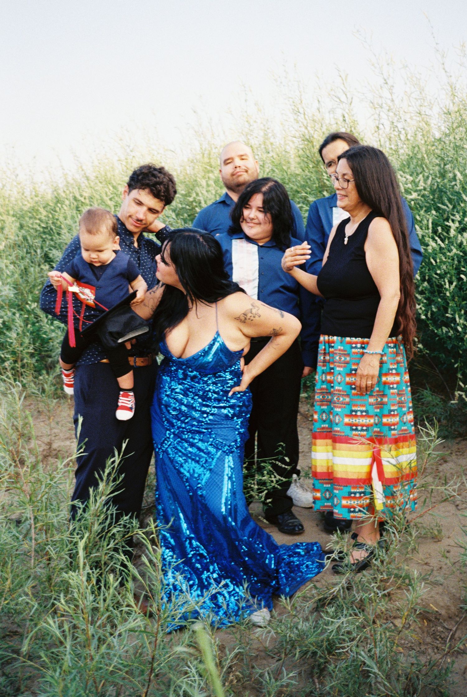 Group gathered in tall grass field wearing mix of formal and casual attire.