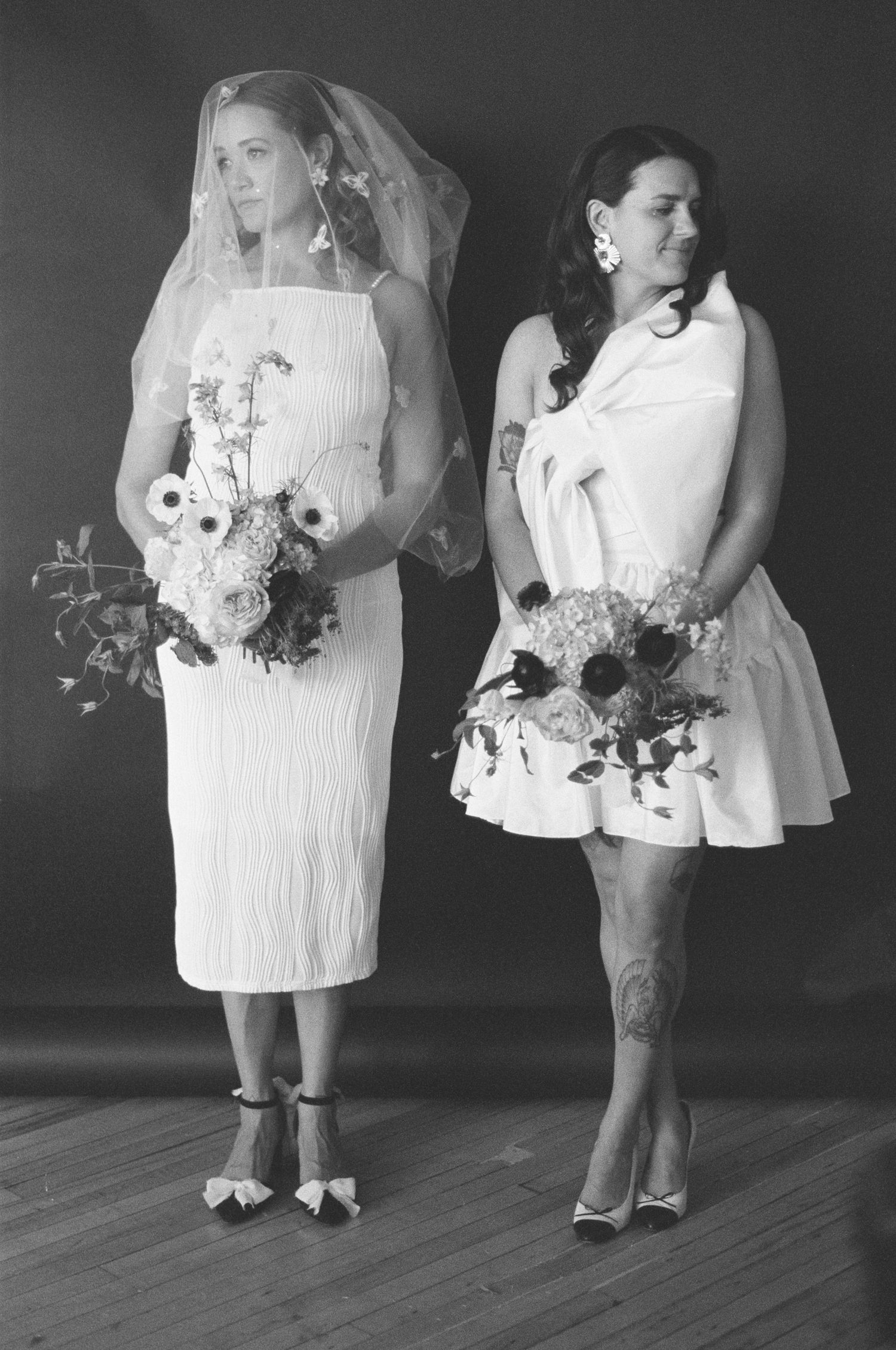 Black and white portrait of two women in white dresses holding floral bouquets with anemones.