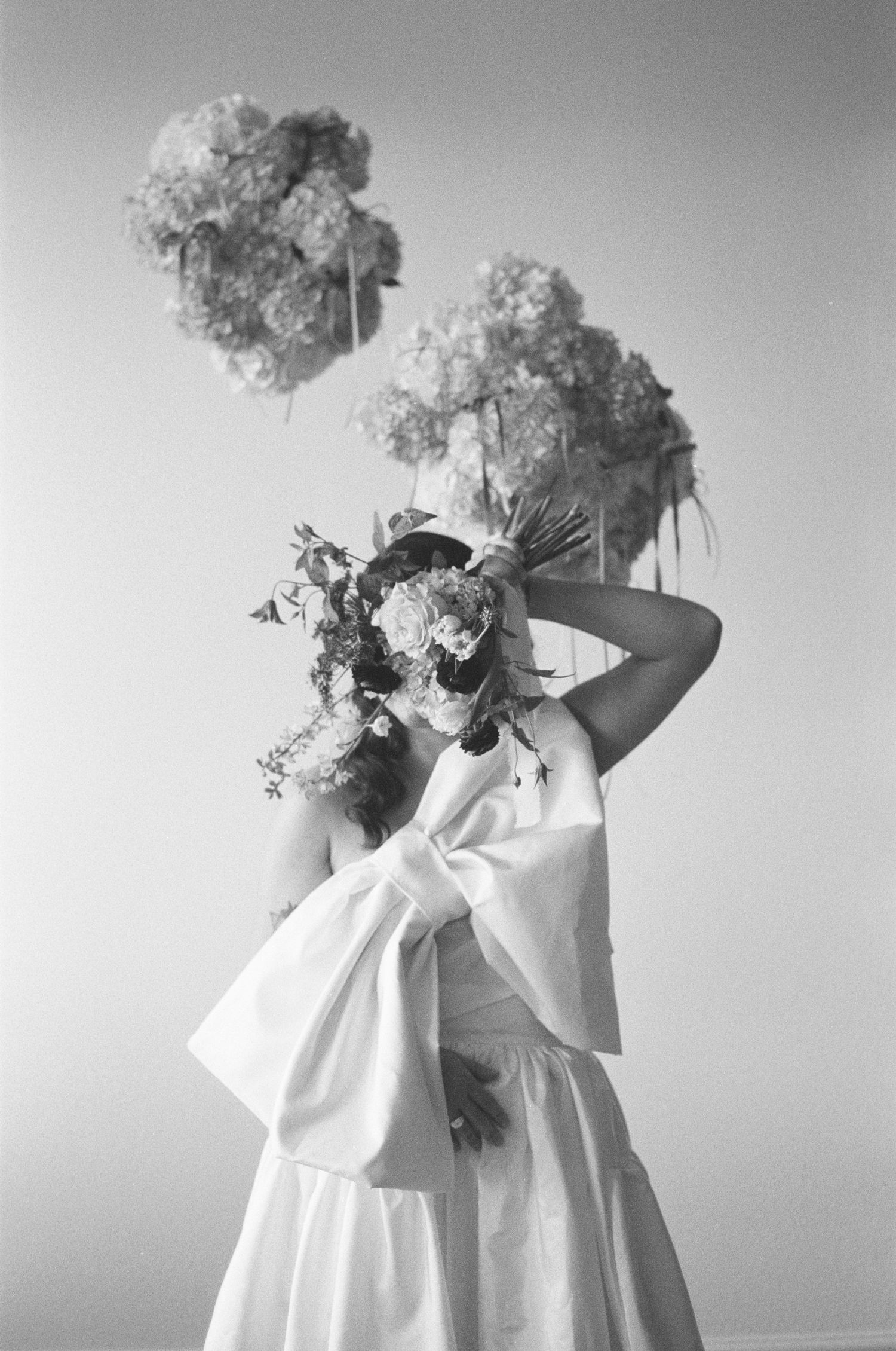 Artistic fashion photo of person in white dress with floral arrangement covering their face.