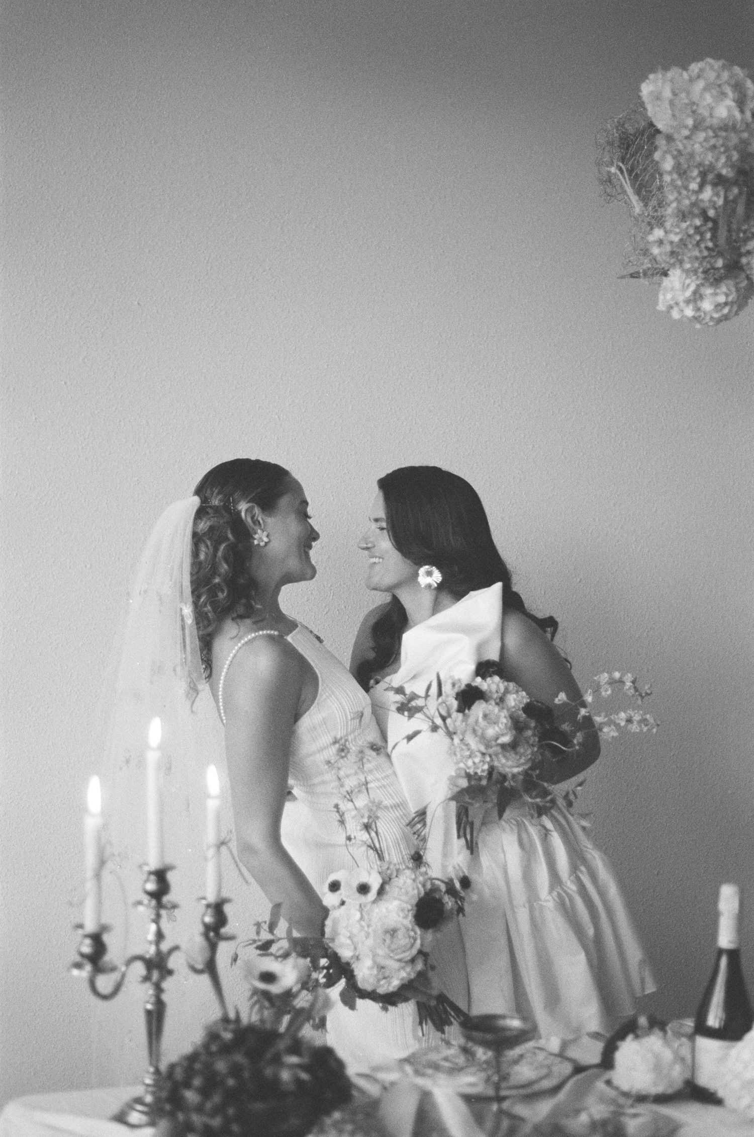 Intimate black and white photo of two people sharing a moment near candles and floral arrangements.
