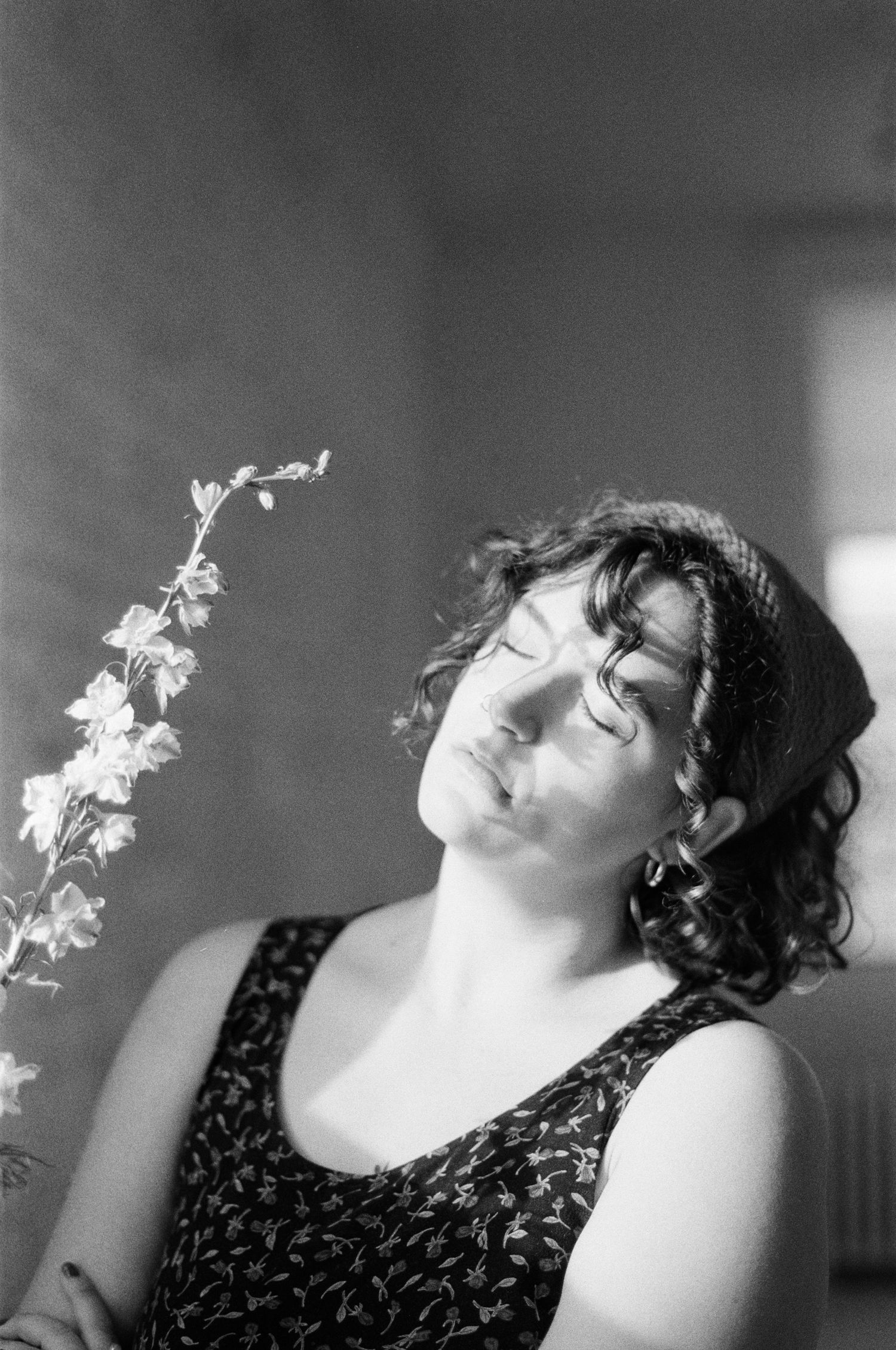 Black and white portrait of person with curly hair holding delicate flower stem against soft lighting.