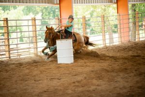 A horse and rider racing around a barrel in a covered arena.