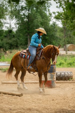 Horse and rider performing around barrel obstacle in dusty training arena.