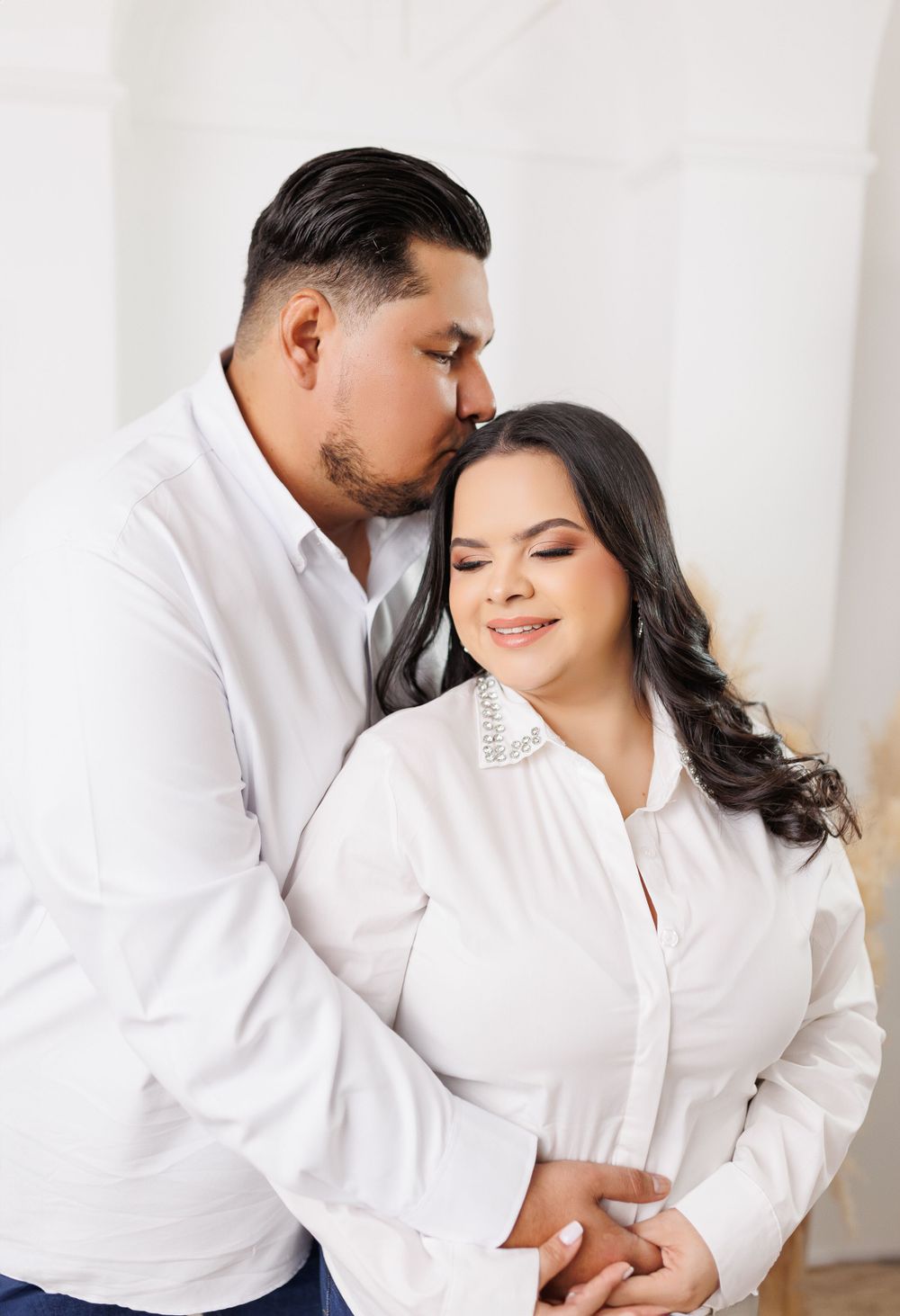 A romantic couple embraces in white shirts against a bright minimal background.