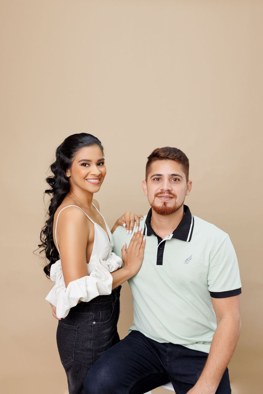 Couple in casual attire sharing intimate moments during studio photo session against beige background.