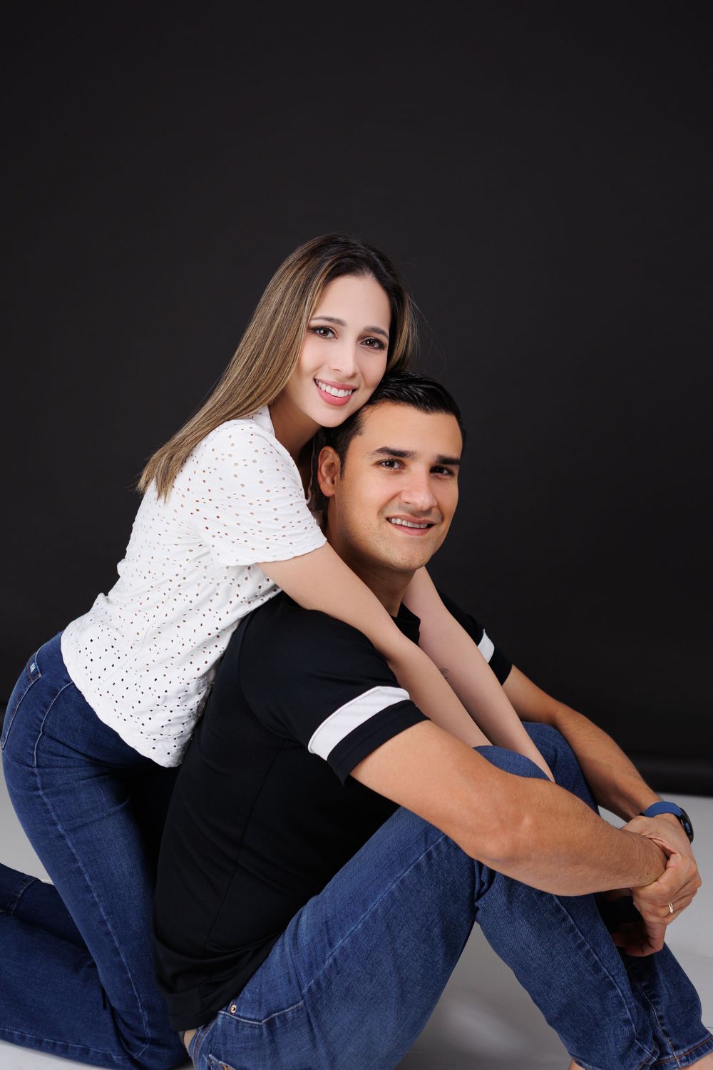 Casual couple pose together against black background in jeans and casual wear.