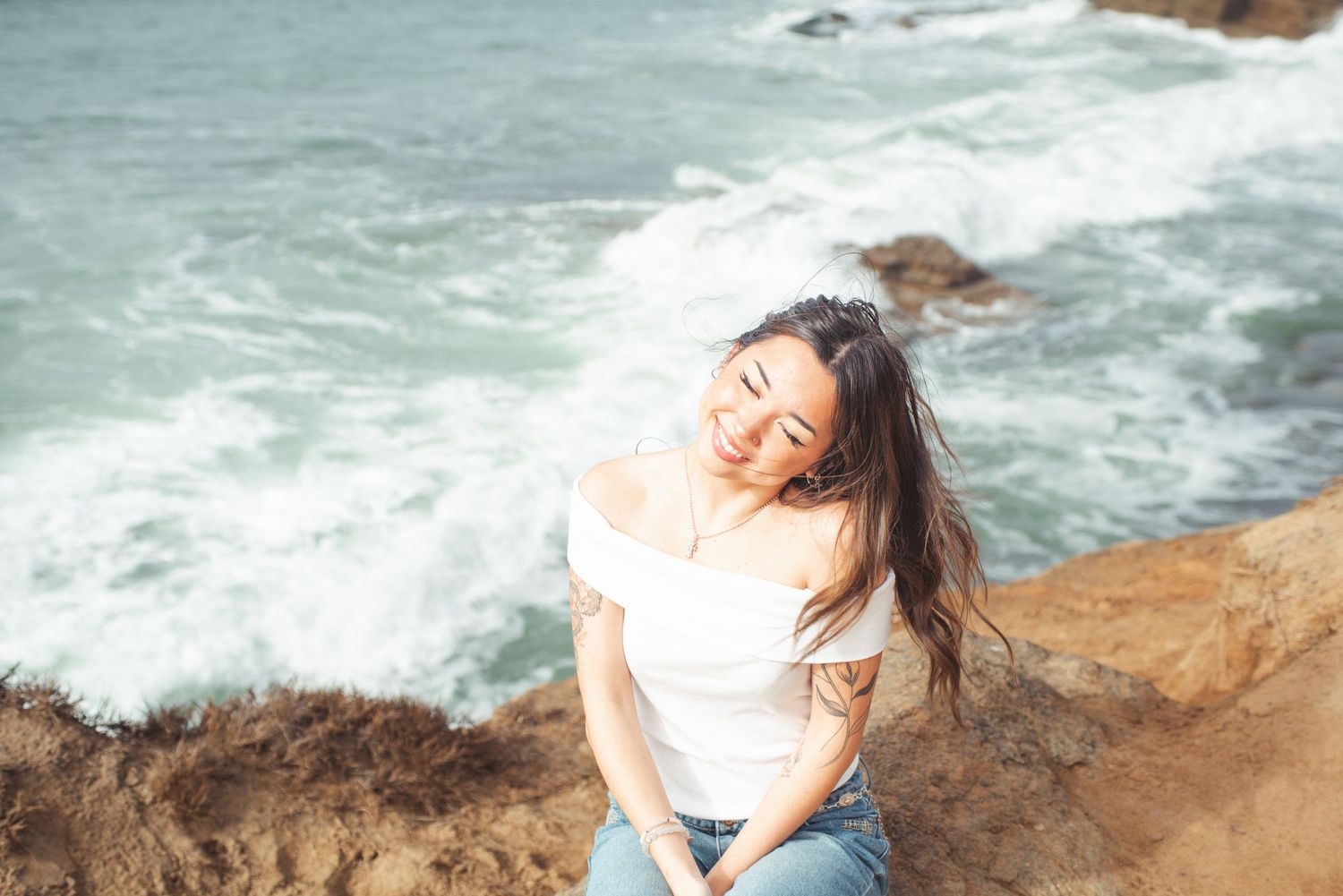 Young women sitting on rock next to cliff and ocean in background