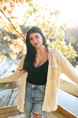 Casual autumn fashion with cream cardigan and jeans photographed in golden sunlight on a wooden deck.