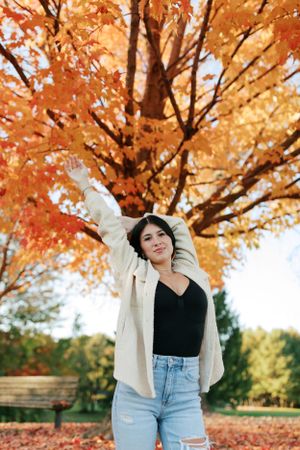 Stylish fall outfit against vibrant orange autumn foliage in a park setting.