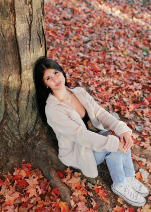 Cozy autumn portrait with cream sweater and jeans among fallen red leaves by a tree trunk.