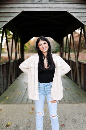 Casual fashion portrait on a covered wooden bridge with cream jacket and distressed jeans.