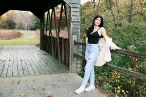 Relaxed pose on covered bridge wearing black top and light denim.