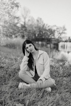 Black and white portrait in casual attire sitting in tall grass by a lake.