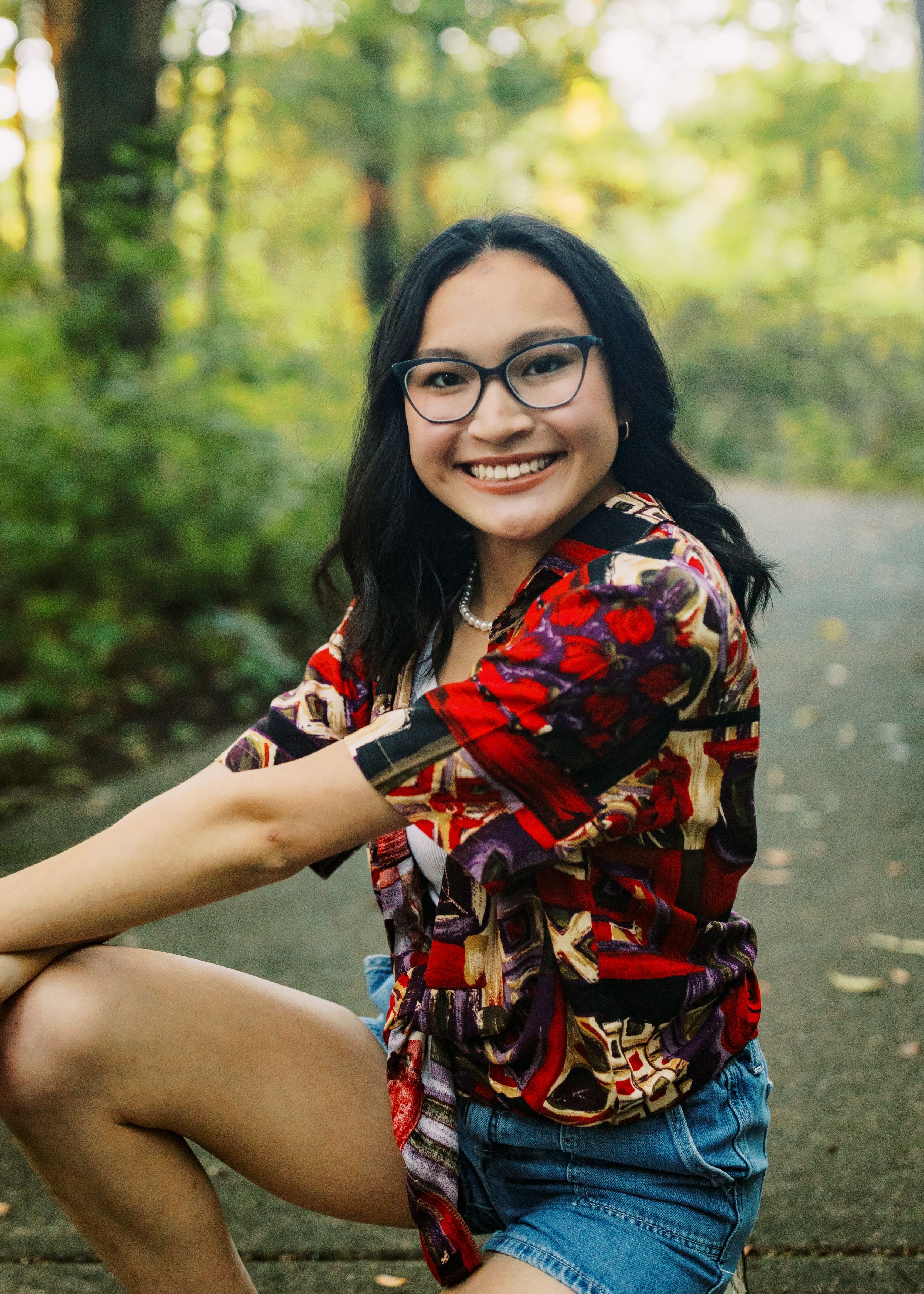 A person wearing glasses and a red floral top poses casually on an outdoor path.