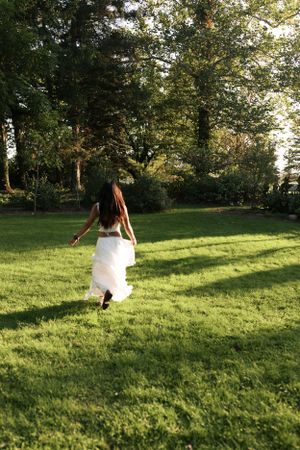 Figure in flowing white dress twirls in sunlit garden with trees in background.