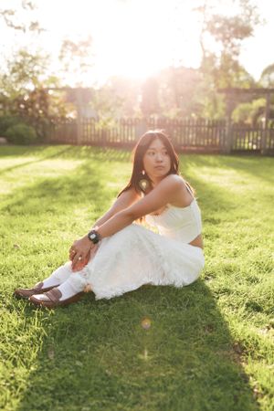 Person in white outfit sits gracefully on sunlit grass during golden hour.