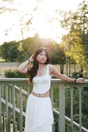 Person in white outfit poses elegantly against railing during sunset.