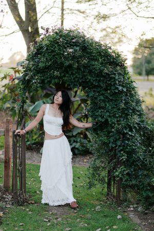 A white lace dress worn under an elegant ivy-covered garden arch in a tranquil outdoor setting.