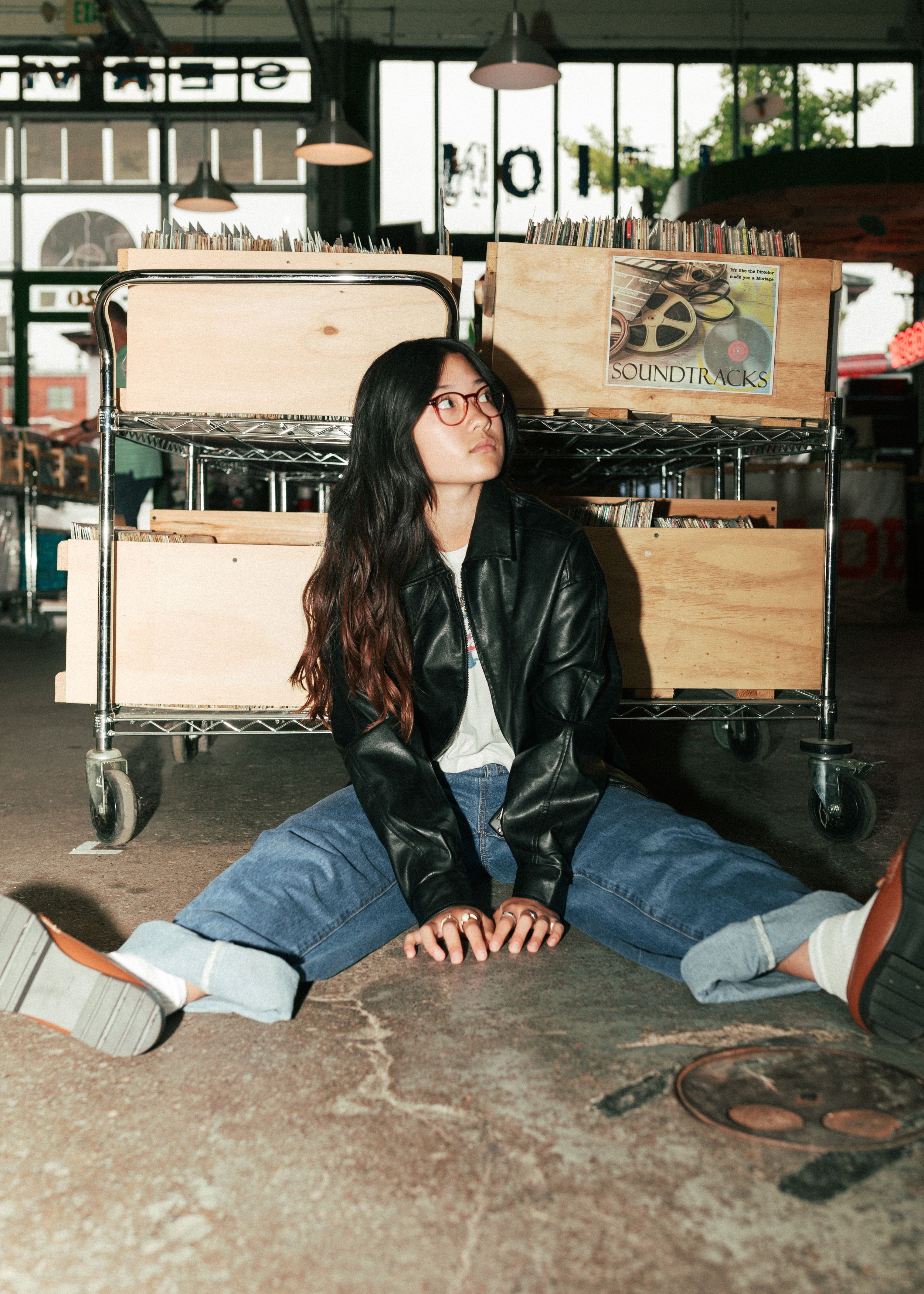 Person in leather jacket sitting on floor of record store.