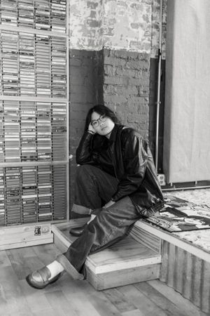 Person in leather jacket relaxing against wall of record store.