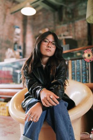 Person in leather jacket sitting casually in vintage chair at record store.