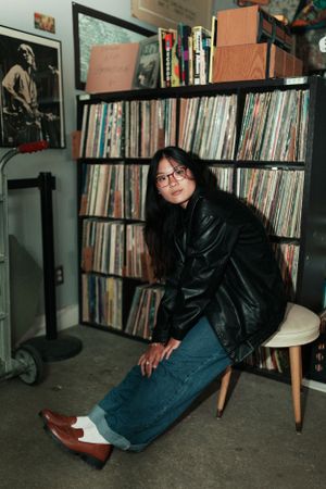 Person in leather jacket poses near large vinyl record collection.