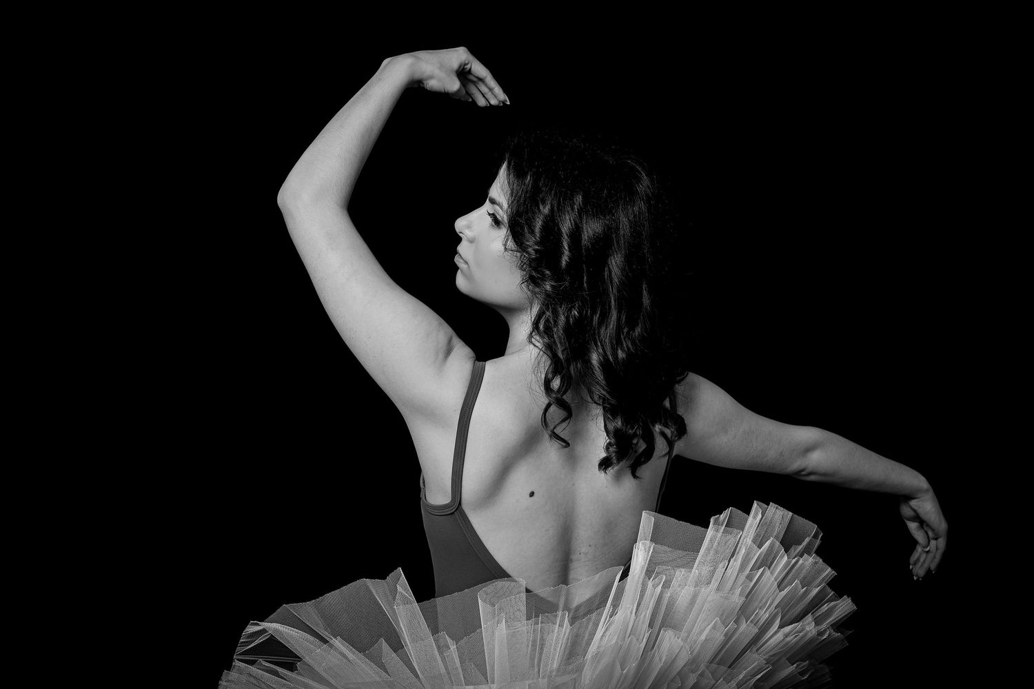 Black and white photo of a ballerina in a tutu posing gracefully against a dark background.