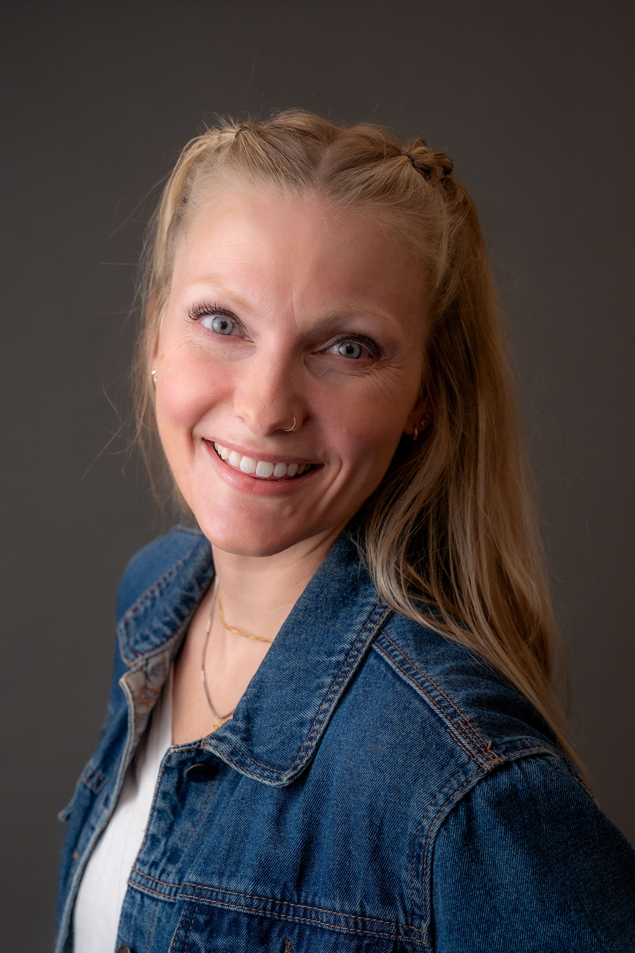 Studio portrait of a person smiling while wearing a denim jacket against a dark background.