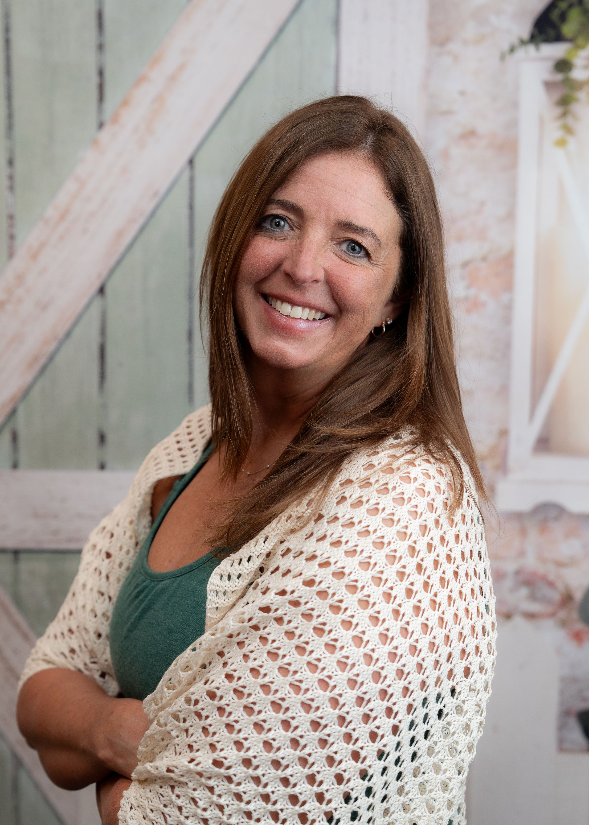 Portrait photo showing someone wearing a cream colored crocheted shawl over a green top against a light background.