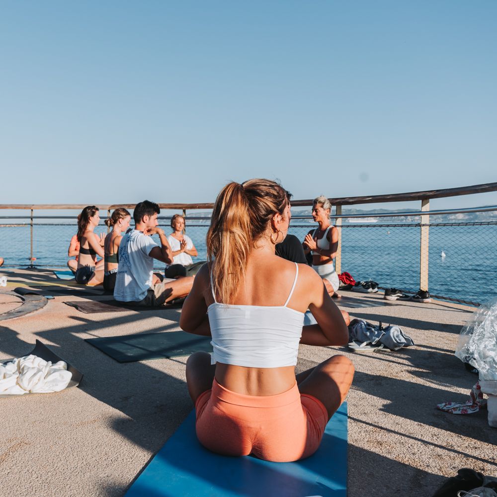 jeune femme de dos qui fait du yoga devant la mer