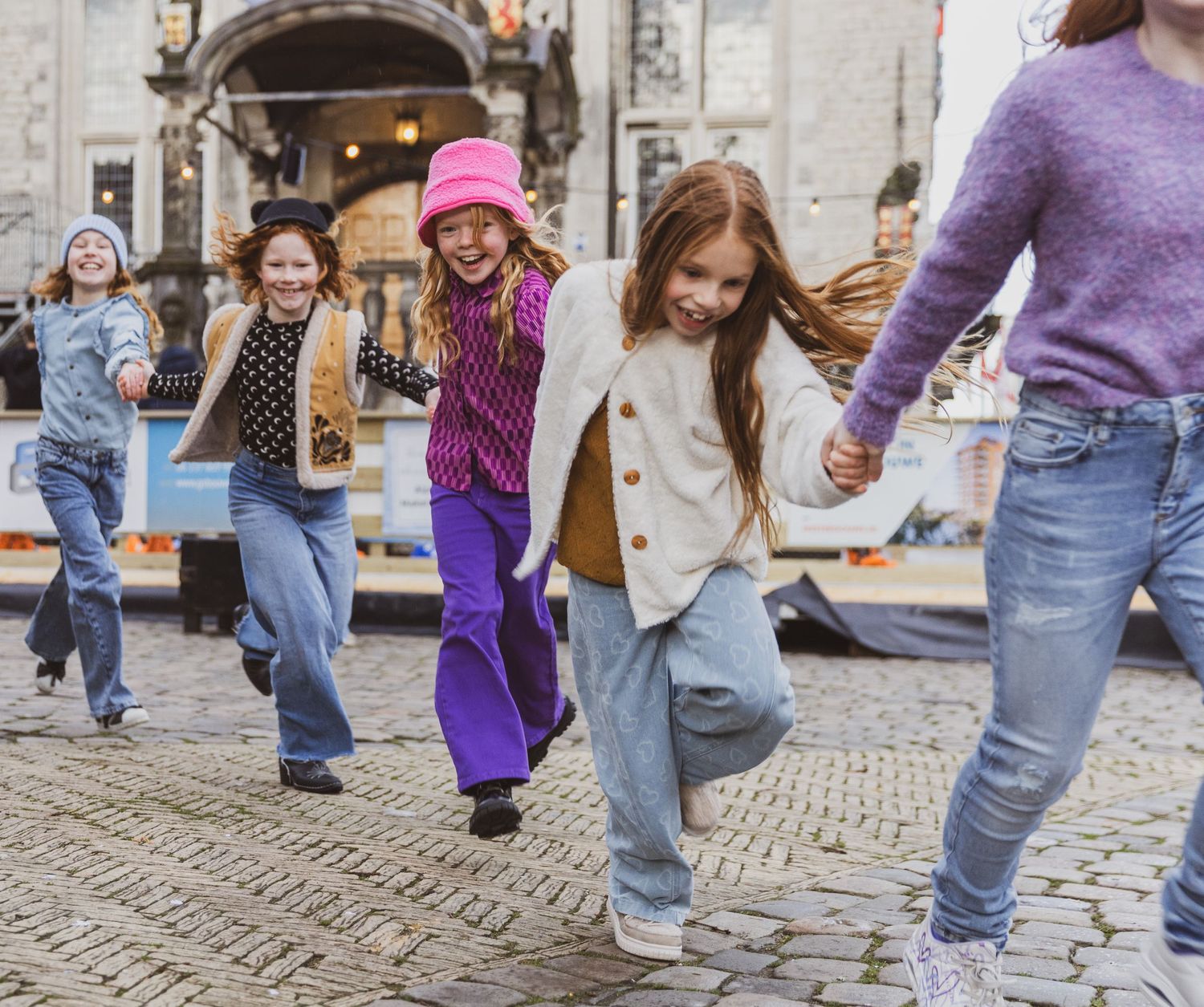 Group of people dancing and jumping joyfully on a cobblestone street in casual attire.