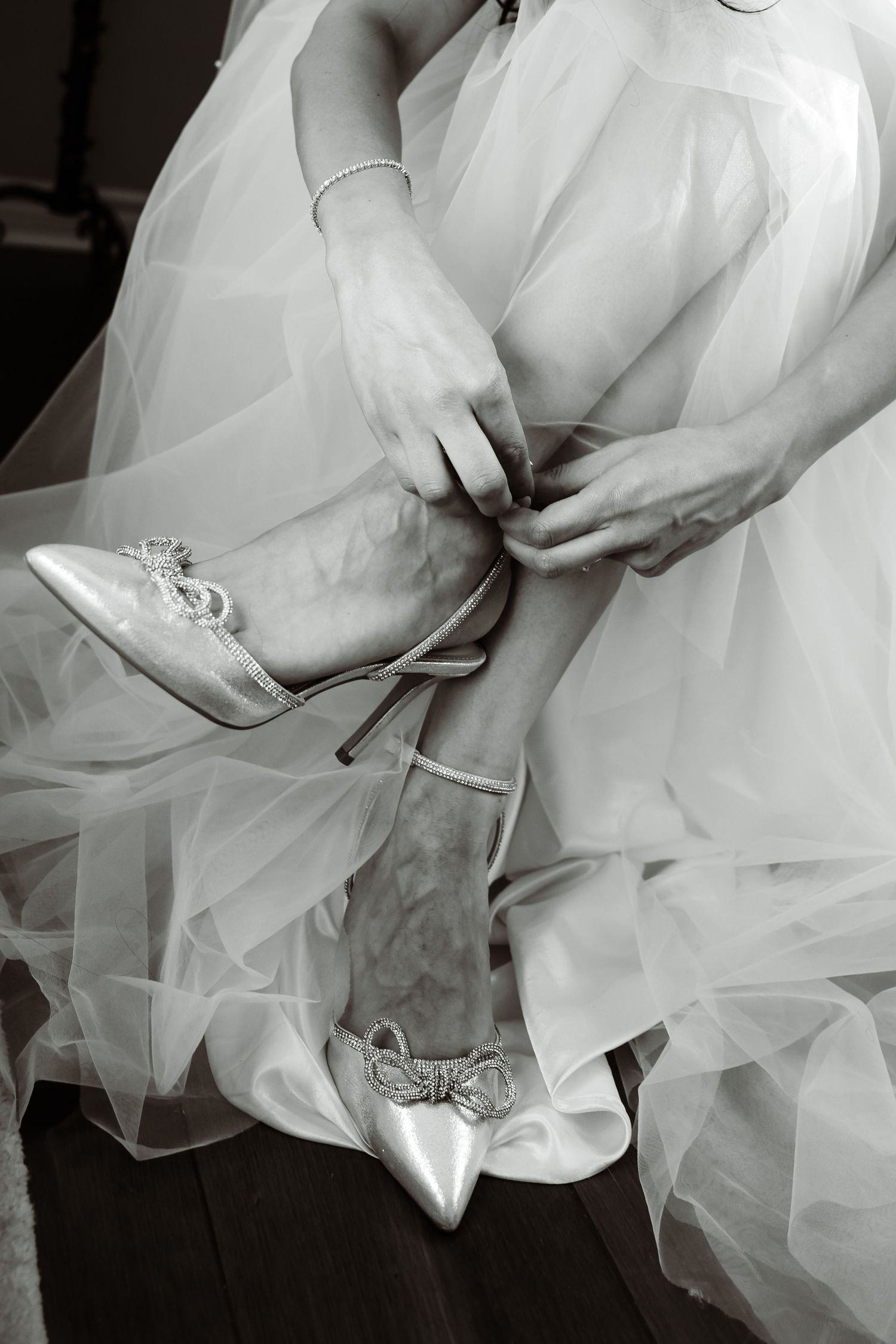 Close-up of bridal shoes being fastened among layers of white tulle wedding dress fabric.