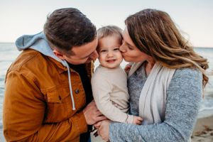 Mother and father kissing toddler on cheek on beach for family session captured by Maryland family photographer Mallory Bramlett.