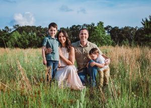Family crouched down posing in green field for family photoshoot captured by Maryland family photographer Mallory Bramlett.