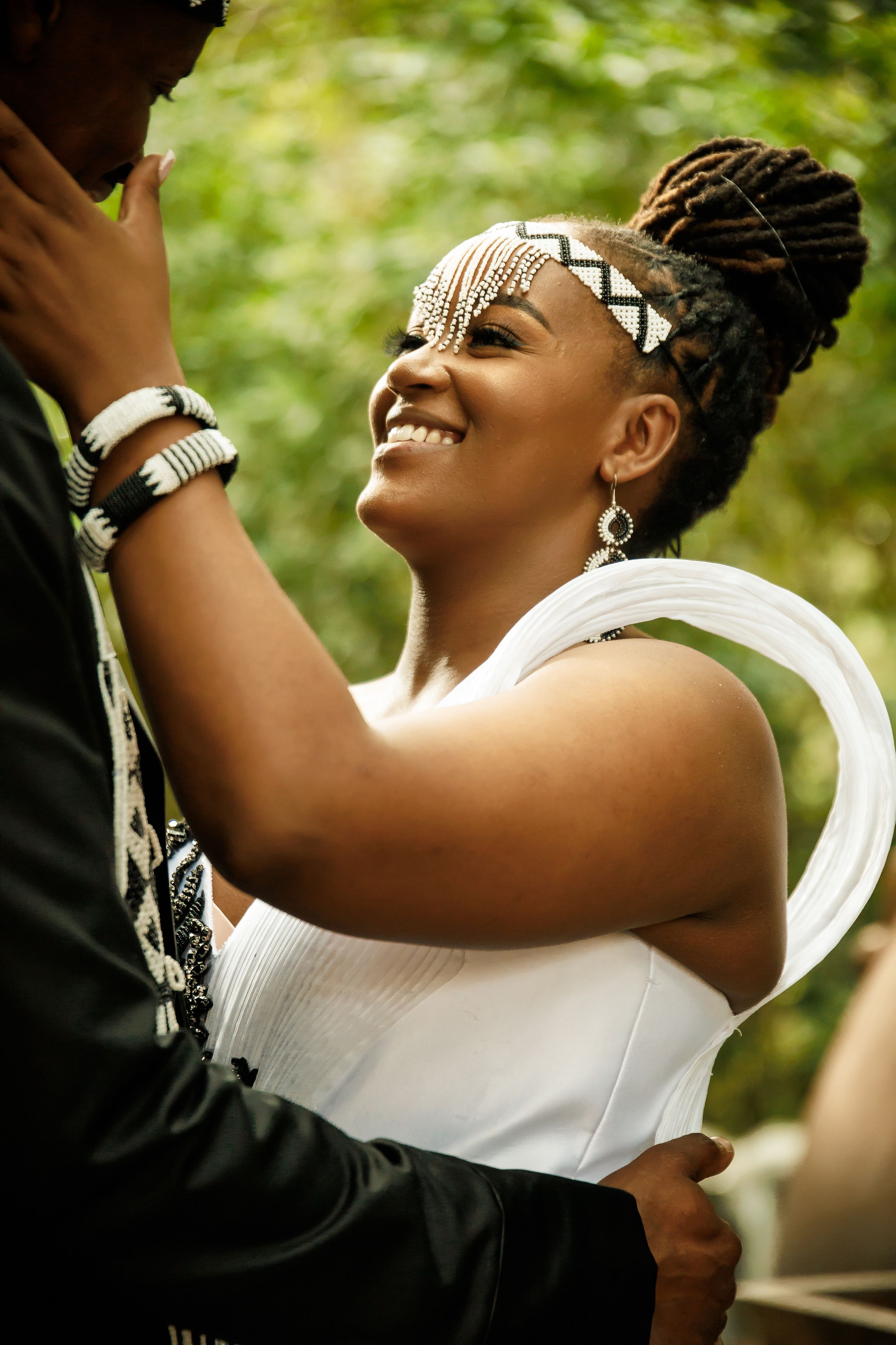 A joyful bride wearing a white dress and beaded headpiece dances outdoors with a natural green background.