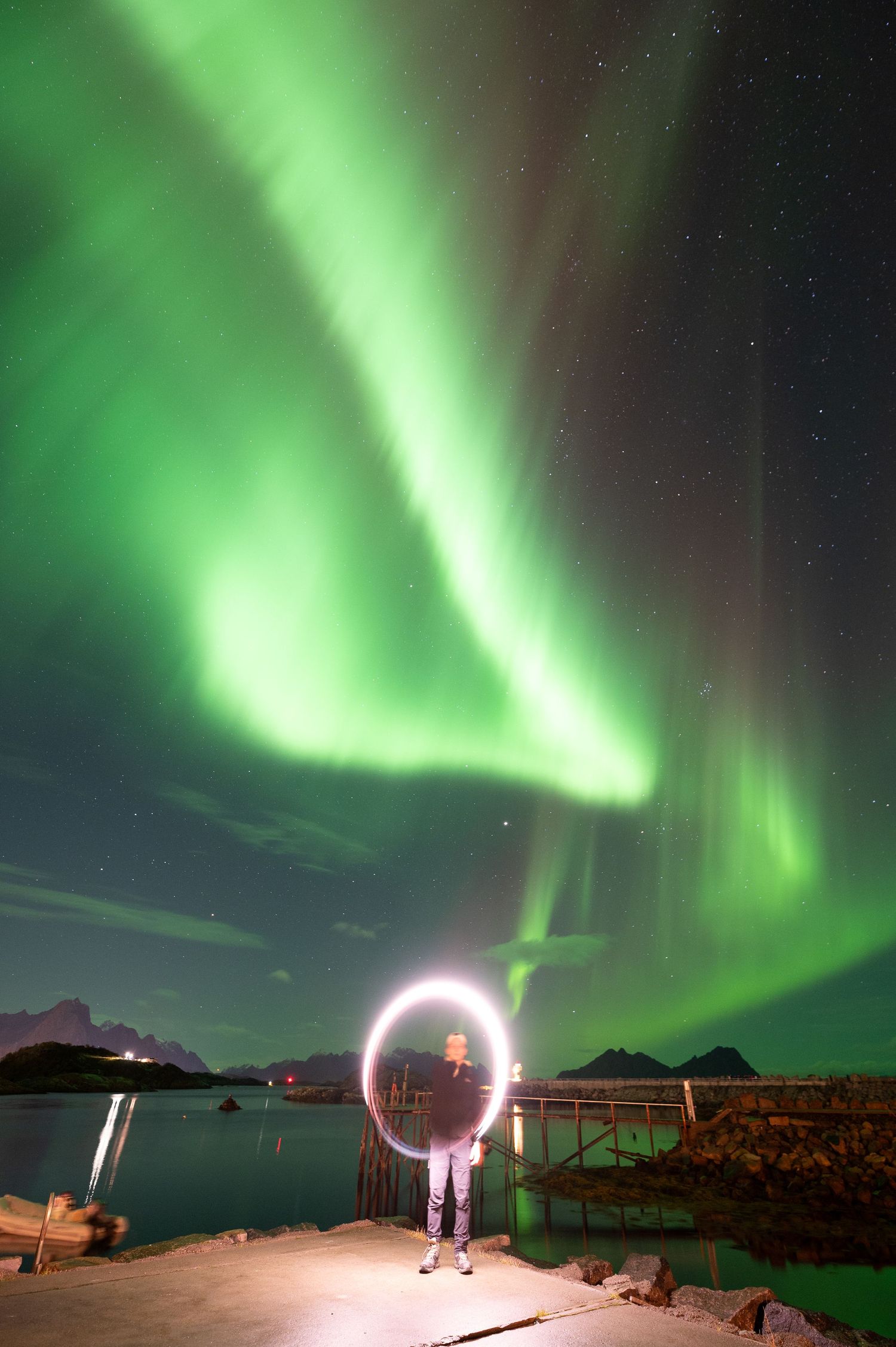 Aurora borealis glows green above a dock with light painting creating a circle in the foreground.