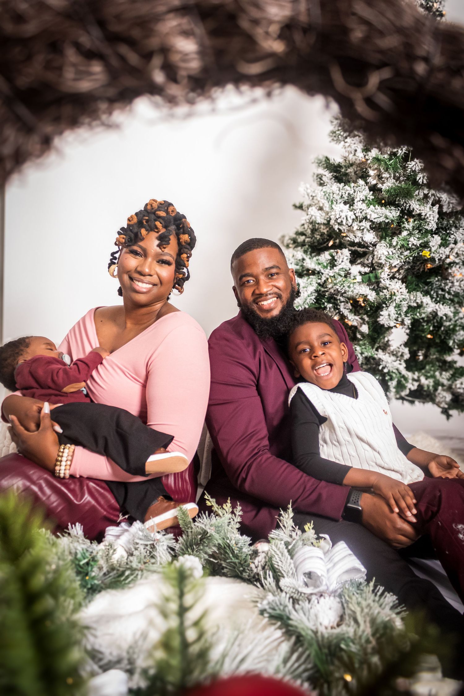 A cozy family holiday portrait surrounded by Christmas decorations and pine branches.