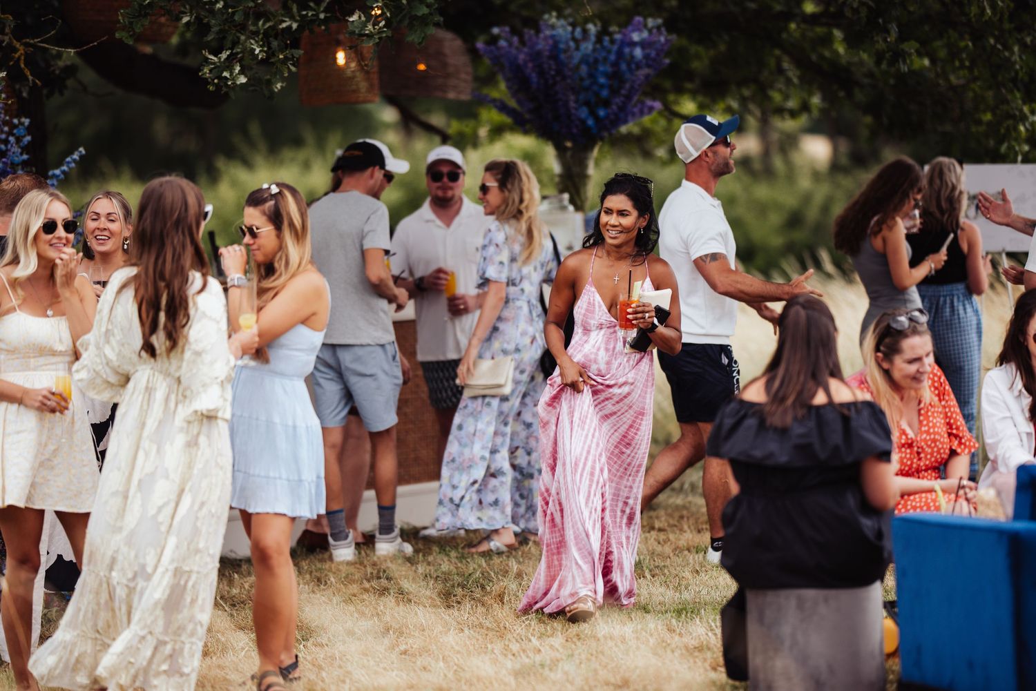 A group of people in summer attire gather outdoors at a casual party event with festive decorations.